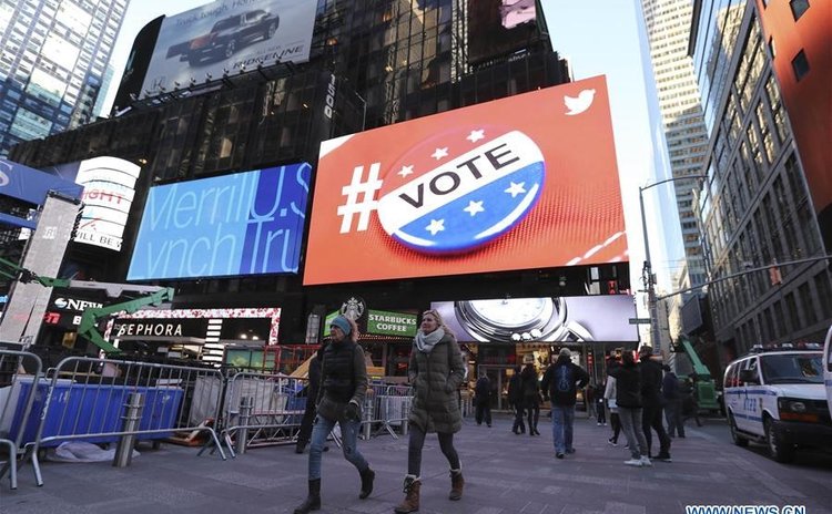 People walk past a screen showing a media advertisement for the voting day at the Times Square in New York, the United States, Nov. 7, 2016. The U.S. general election will be held on Nov. 8. (Xinhua/W