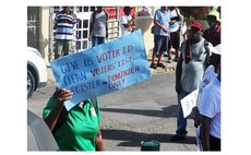 Woman holds up a sign during electoral reform march in Roseau in August 2023